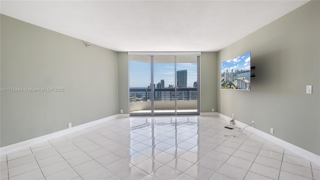 empty room with light tile patterned floors, a wall of windows, baseboards, and a city view