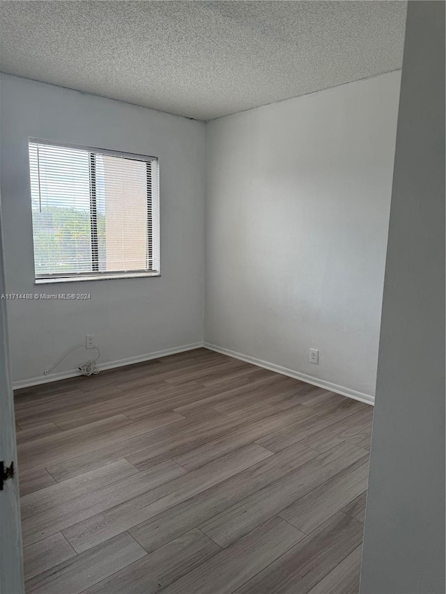 empty room with a textured ceiling and light hardwood / wood-style flooring