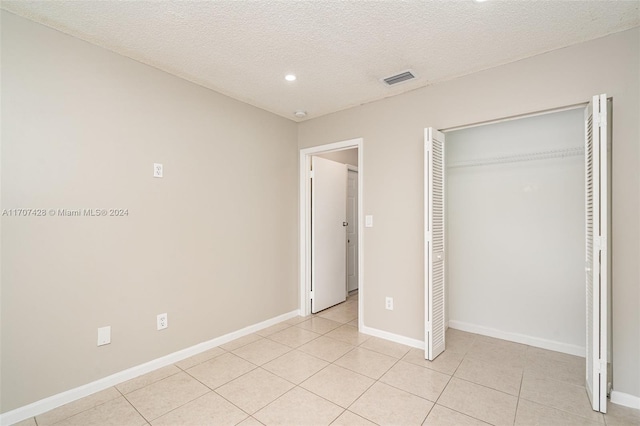 unfurnished bedroom featuring a closet, light tile patterned flooring, and a textured ceiling