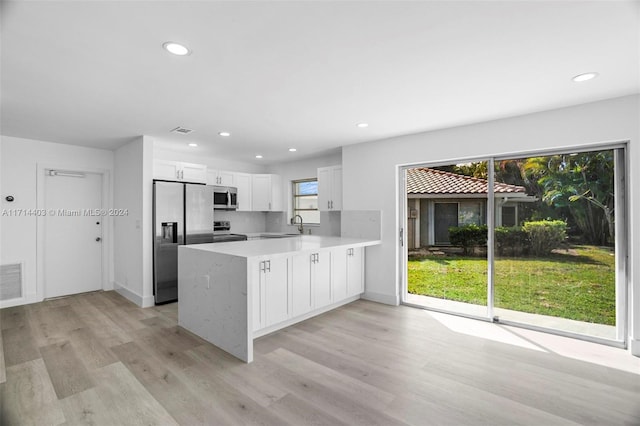 kitchen featuring kitchen peninsula, appliances with stainless steel finishes, decorative backsplash, white cabinets, and light hardwood / wood-style floors