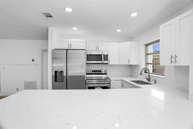 kitchen with white cabinetry, sink, light stone countertops, backsplash, and appliances with stainless steel finishes