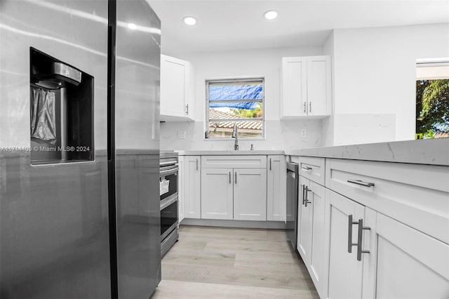 kitchen with sink, tasteful backsplash, light hardwood / wood-style floors, white cabinets, and appliances with stainless steel finishes