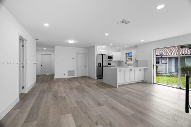 kitchen with kitchen peninsula, appliances with stainless steel finishes, sink, white cabinets, and light hardwood / wood-style floors