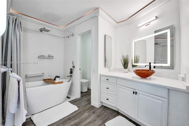 bathroom with a washtub, wood-type flooring, toilet, vanity, and ornamental molding