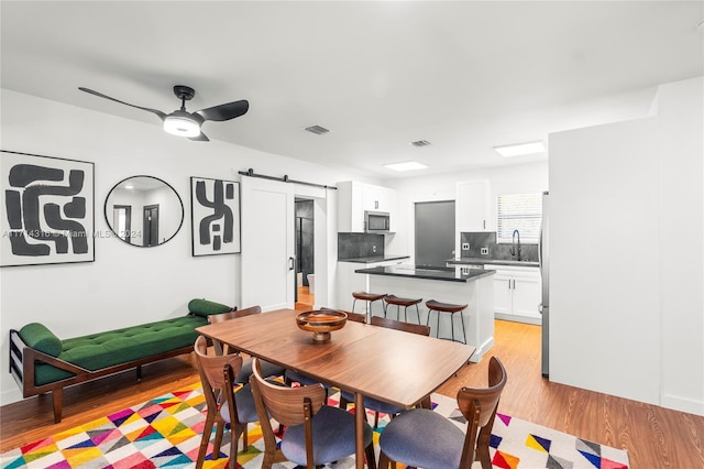 dining space featuring ceiling fan, a barn door, light wood-type flooring, and sink