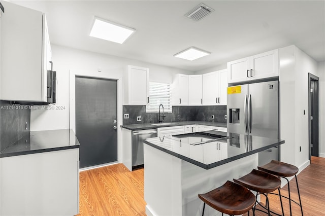 kitchen featuring sink, light hardwood / wood-style floors, a kitchen bar, white cabinetry, and stainless steel appliances