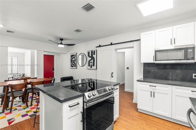 kitchen featuring tasteful backsplash, stainless steel appliances, a barn door, white cabinets, and light hardwood / wood-style floors