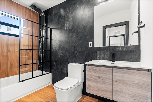 full bathroom with vanity, shower / bath combination with glass door, wood-type flooring, tile walls, and toilet