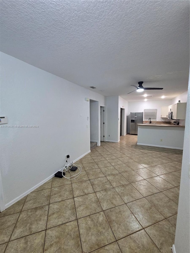 unfurnished living room with ceiling fan, light tile patterned floors, and a textured ceiling