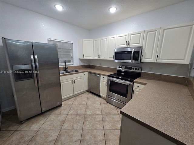 kitchen with sink, stainless steel appliances, light tile patterned floors, a textured ceiling, and white cabinets