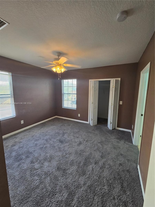 unfurnished bedroom featuring a textured ceiling, dark carpet, and ceiling fan