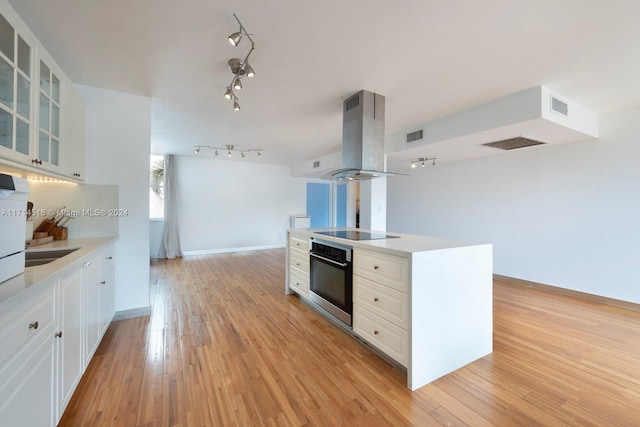 kitchen featuring stainless steel oven, island range hood, white cabinets, black electric stovetop, and light hardwood / wood-style floors