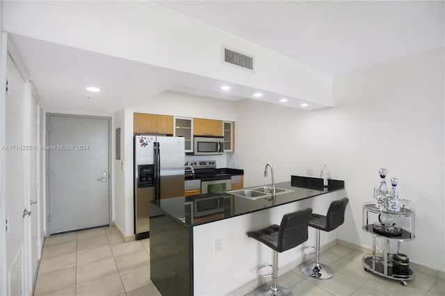 kitchen featuring sink, light tile patterned floors, appliances with stainless steel finishes, kitchen peninsula, and a breakfast bar area