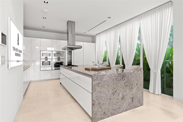 kitchen with white cabinetry, stainless steel gas cooktop, island exhaust hood, dark stone counters, and a kitchen island