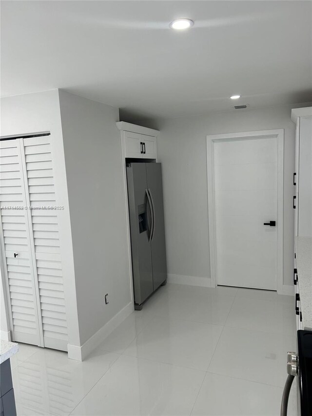 interior space featuring stainless steel fridge, white cabinetry, and light tile patterned floors