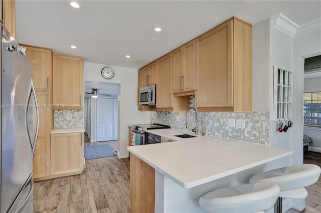 kitchen with sink, kitchen peninsula, light hardwood / wood-style floors, a breakfast bar area, and appliances with stainless steel finishes