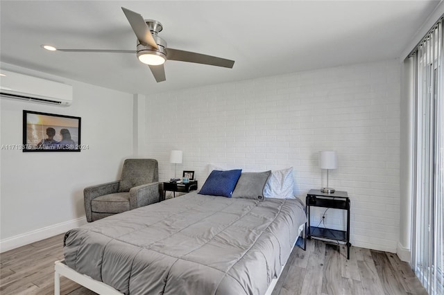 bedroom with brick wall, light wood-type flooring, a wall mounted AC, and ceiling fan