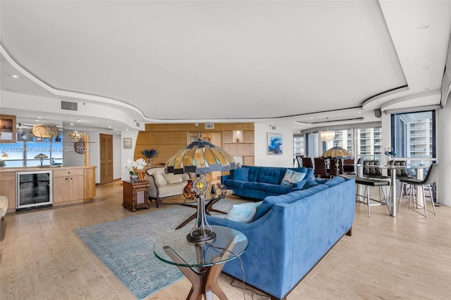 living room with a tray ceiling, beverage cooler, and light wood-type flooring