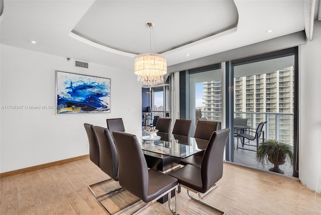 dining room with a chandelier, light hardwood / wood-style floors, and a raised ceiling