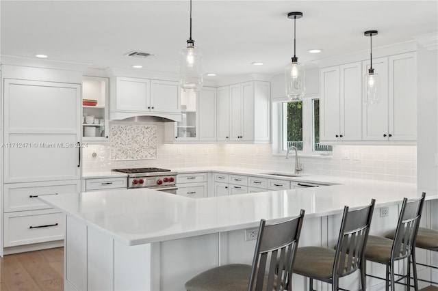 kitchen featuring white cabinets, a kitchen bar, high end range, and sink