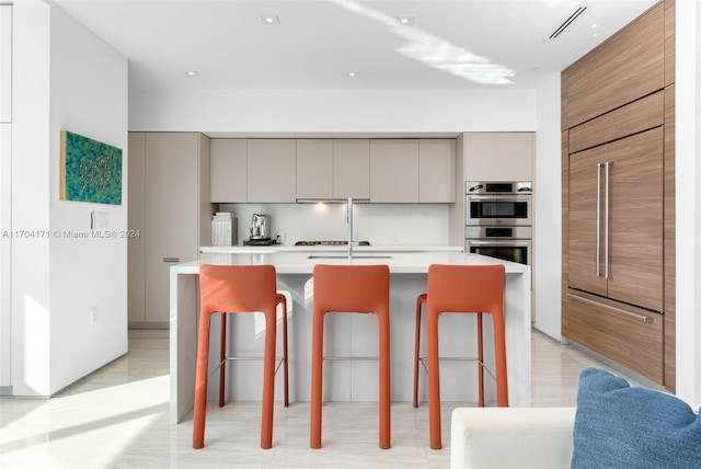 kitchen featuring a center island with sink, a kitchen breakfast bar, and gray cabinetry