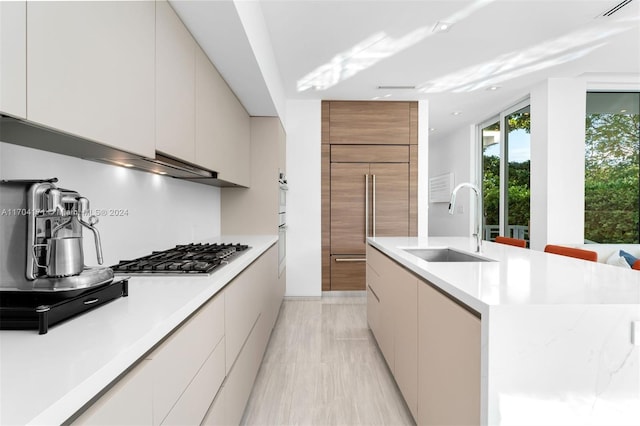 kitchen featuring a center island, sink, paneled built in refrigerator, double oven, and stainless steel gas cooktop