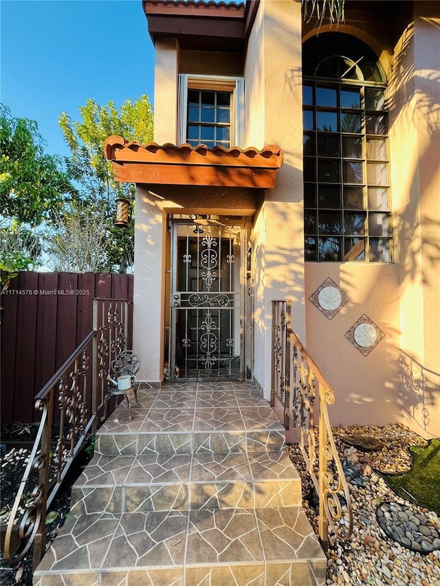 entrance to property featuring a tile roof, fence, and stucco siding