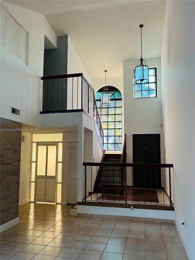 interior space with a textured ceiling, a high ceiling, visible vents, and tile patterned floors