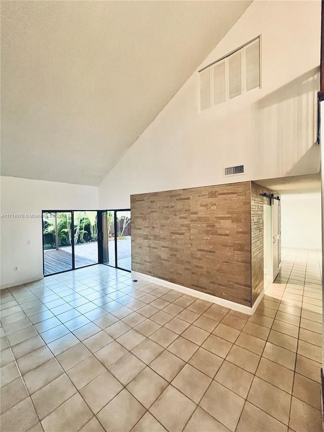 unfurnished room with light tile patterned floors, a barn door, visible vents, and high vaulted ceiling