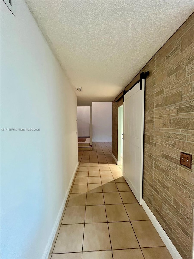 hallway with light tile patterned flooring, a textured ceiling, brick wall, and a barn door