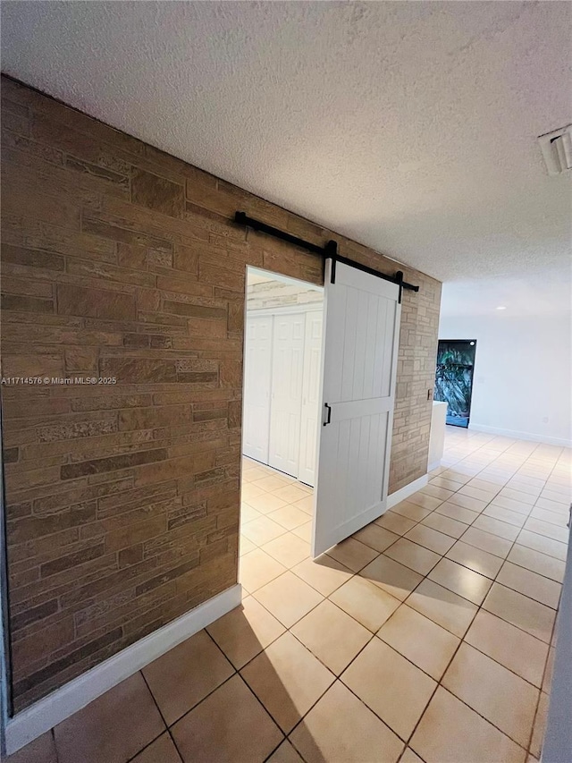 spare room with light tile patterned floors, a textured ceiling, a barn door, wooden walls, and baseboards