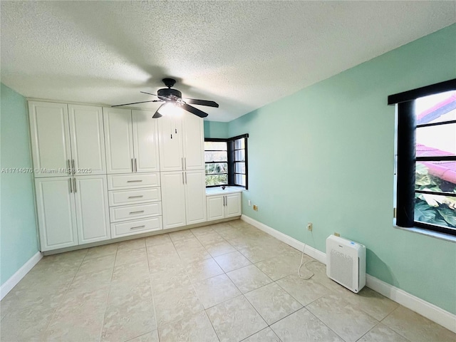 unfurnished bedroom with ceiling fan, light tile patterned floors, a textured ceiling, and baseboards