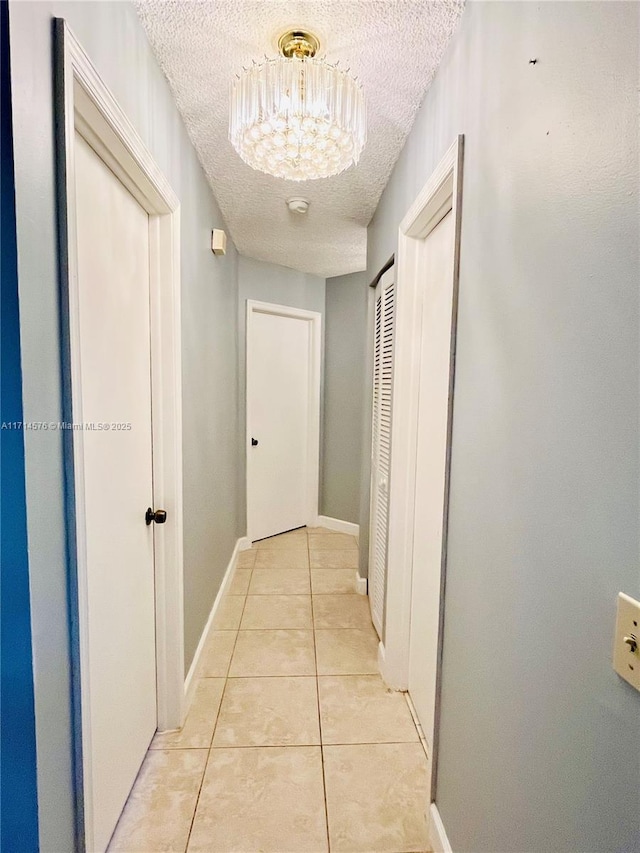 hallway with a textured ceiling, light tile patterned flooring, baseboards, and an inviting chandelier