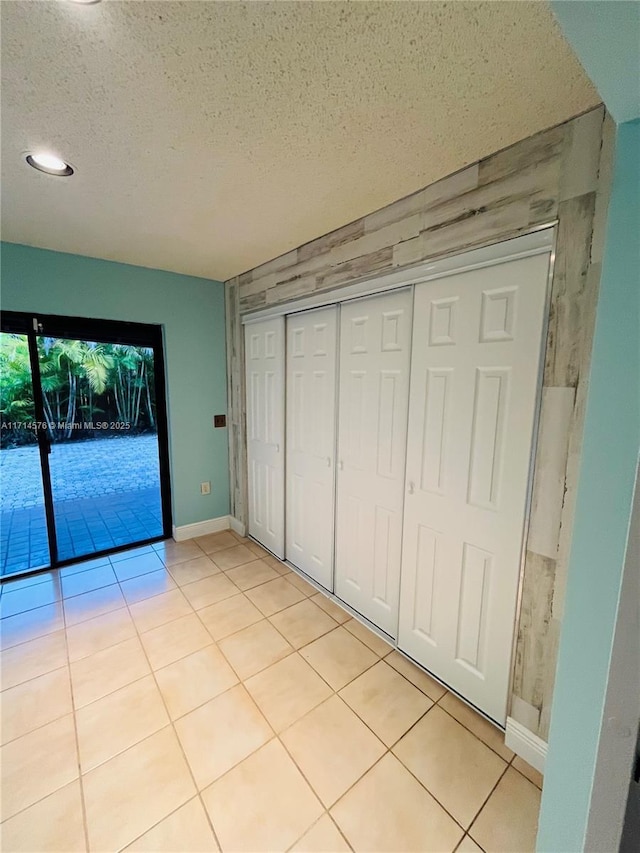 unfurnished bedroom with a closet, a textured ceiling, baseboards, and light tile patterned floors