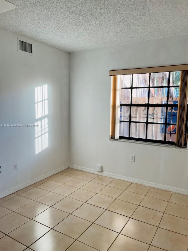 empty room featuring visible vents, a textured ceiling, and baseboards