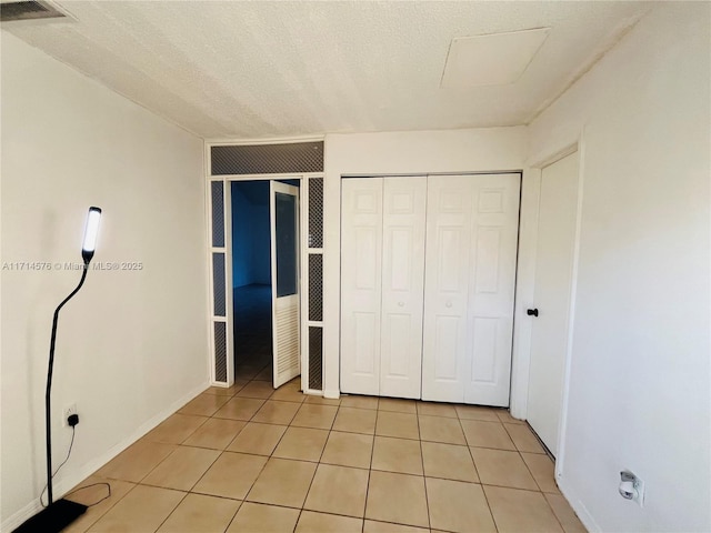 unfurnished bedroom with a closet, visible vents, a textured ceiling, and light tile patterned floors