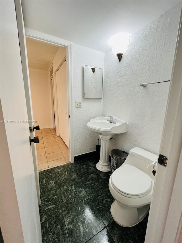 half bath with a textured wall, a sink, and toilet