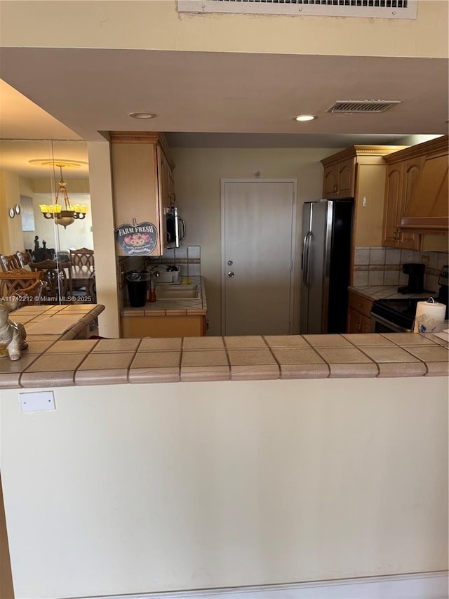 kitchen with tasteful backsplash, black electric range oven, custom exhaust hood, stainless steel refrigerator, and tile counters