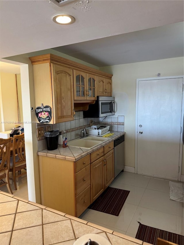 kitchen featuring sink, decorative backsplash, light tile patterned floors, appliances with stainless steel finishes, and tile counters