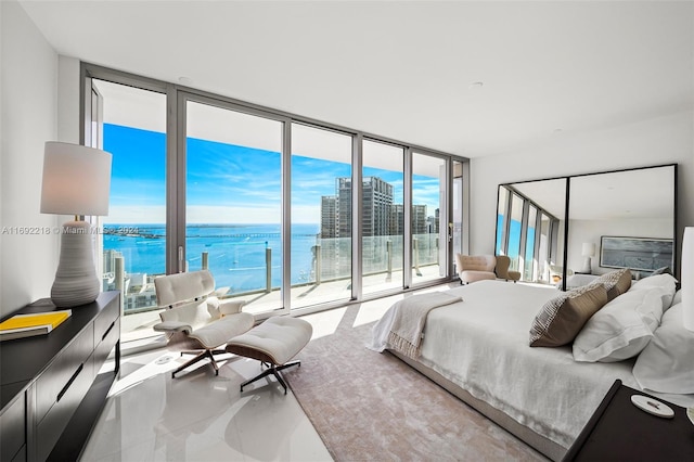 bedroom featuring access to exterior, a water view, and a wall of windows