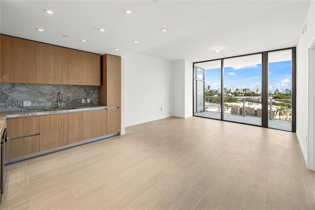 kitchen featuring backsplash, sink, light hardwood / wood-style flooring, and a wall of windows