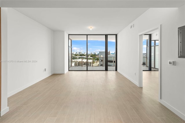 empty room featuring a wall of windows and light hardwood / wood-style flooring