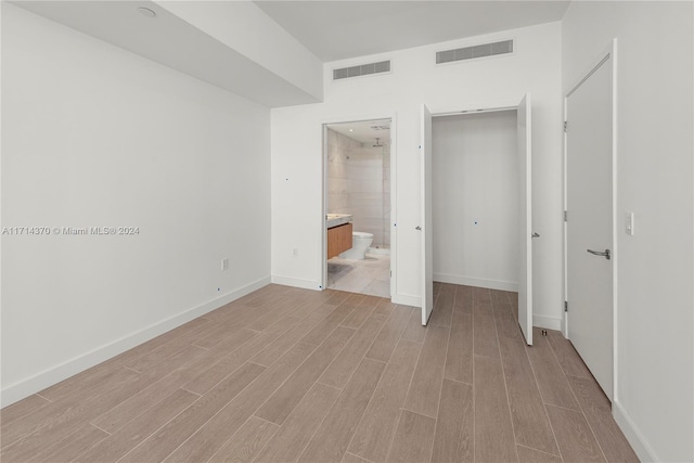 unfurnished bedroom featuring light hardwood / wood-style floors, a closet, and ensuite bath