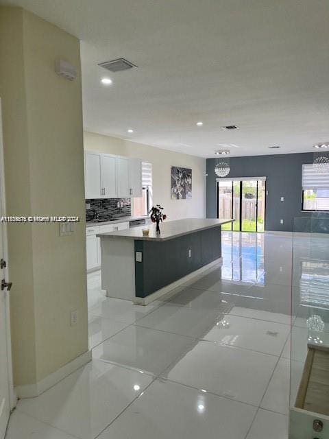 kitchen featuring decorative backsplash, white cabinetry, a kitchen island with sink, and light tile patterned flooring