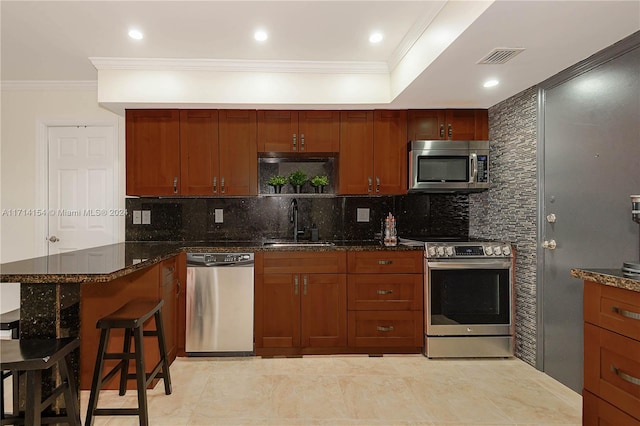 kitchen featuring dark stone counters, stainless steel appliances, crown molding, sink, and a breakfast bar area