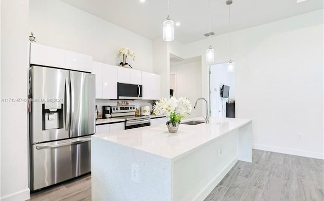 kitchen with a kitchen island with sink, sink, decorative light fixtures, white cabinetry, and stainless steel appliances