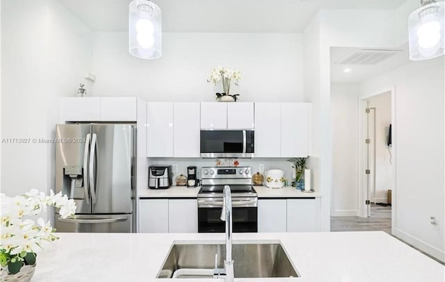 kitchen featuring decorative backsplash, appliances with stainless steel finishes, sink, white cabinets, and hanging light fixtures