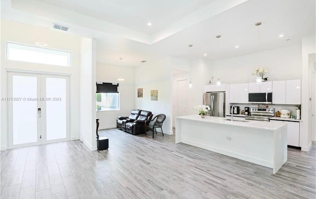 kitchen featuring appliances with stainless steel finishes, french doors, a kitchen island with sink, sink, and decorative light fixtures