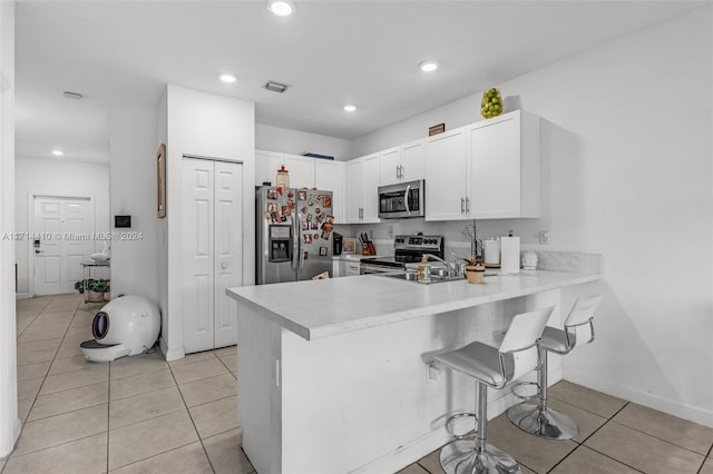 kitchen with kitchen peninsula, a kitchen breakfast bar, stainless steel appliances, light tile patterned floors, and white cabinetry