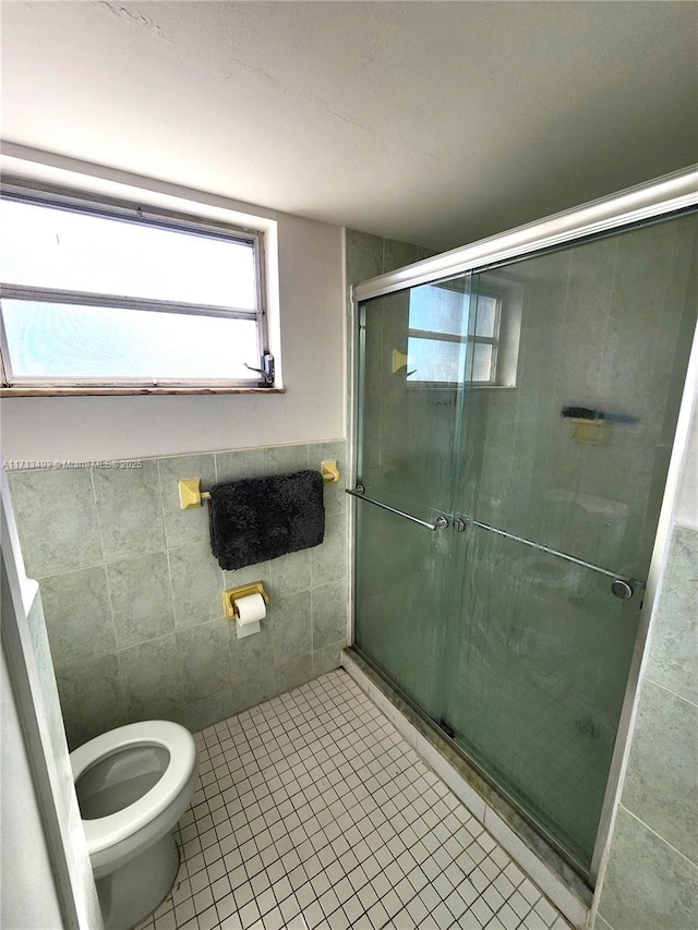 bathroom featuring a stall shower, wainscoting, toilet, tile patterned floors, and tile walls